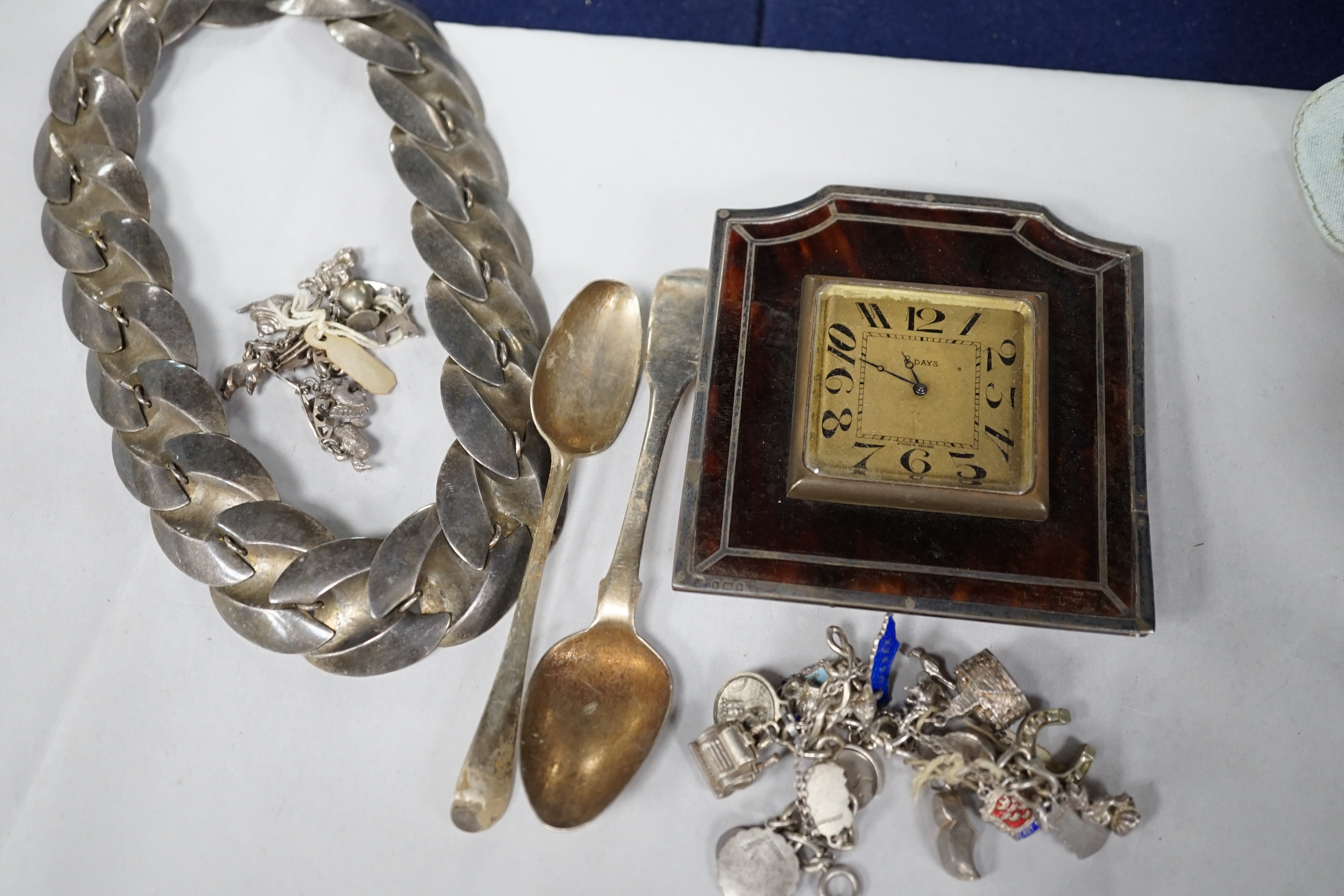 A silver charm bracelet, hung with assorted charms, some hallmarked, one other white metal charm bracelet, a stylish white metal necklace, two silver teaspoons and a George V silver and tortoiseshell mounted timepiece, L